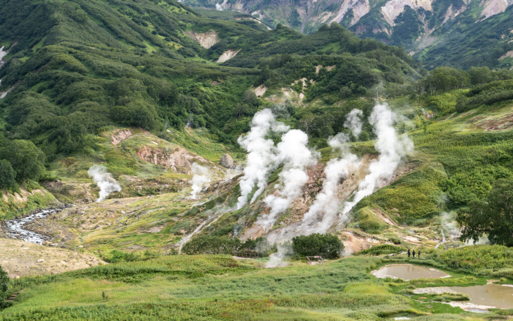 Lush green valley with mountains and white smoke rising showcasing natural energy wallpaper