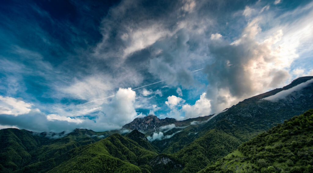 Lush green mountains and dense forest under dramatic swirling cloud sky vibrant nature wallpaper
