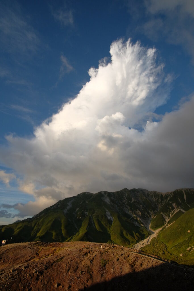 Lush green mountains and rugged peaks under vibrant blue sky with billowing white clouds Wallpaper