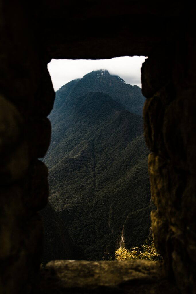 Lush forested mountain peak seen through ancient stone window with deep green shadows wallpaper