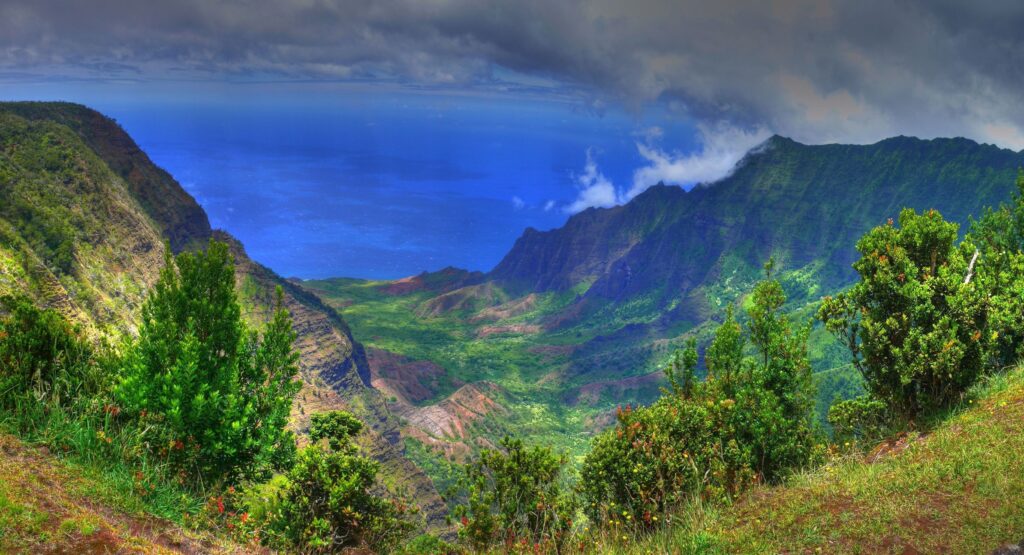 Vast mountain valley with lush greenery and deep blue horizon under dramatic cloudy sky wallpaper