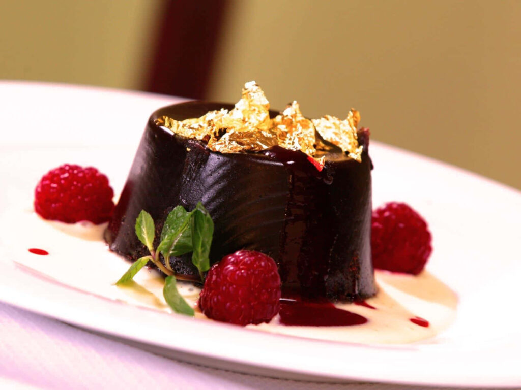 Rich chocolate cake with gold leaf fresh raspberries mint and creamy sauce on elegant plate Wallpaper