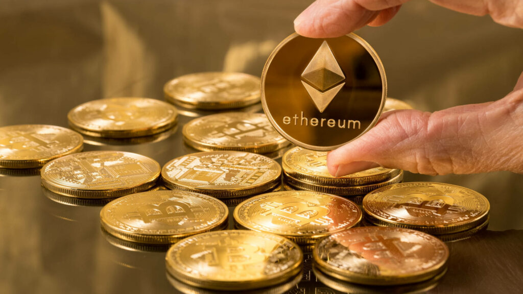 Hand holding shiny Ethereum gold coin above scattered gold coins luxury crypto wallpaper background