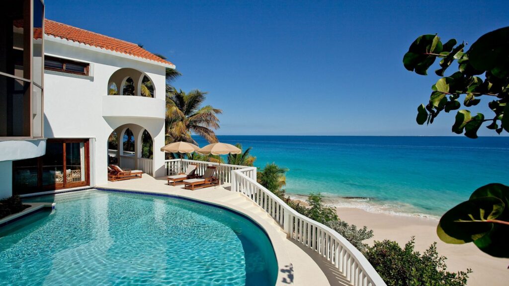 Luxurious hacienda villa by pool overlooking turquoise sea and pristine beach under blue sky Wallpaper
