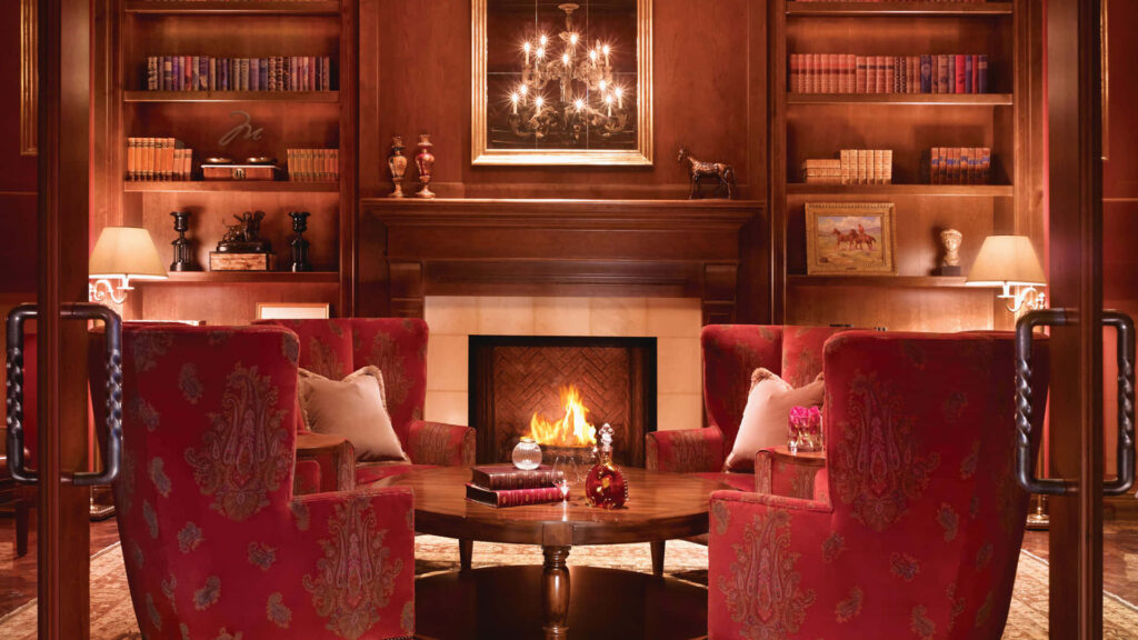 Luxurious library room with red armchairs fireplace wooden bookshelves elegant décor warm lighting Wallpaper