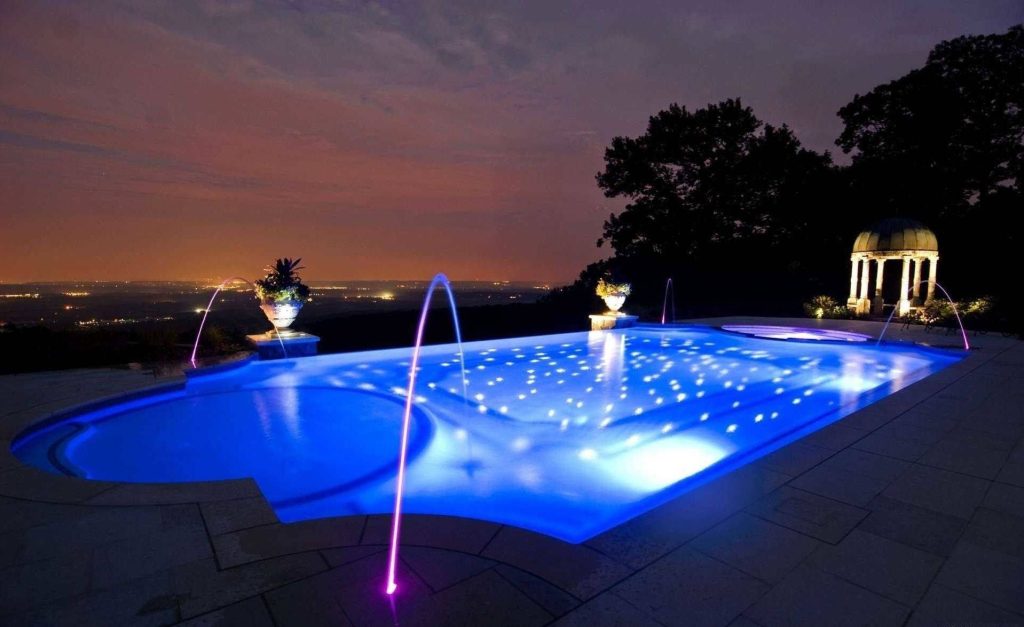 Luxurious night pool with blue LEDs floating lights fountains and city skyline gazebo view Wallpaper