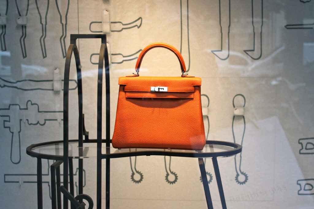 Luxurious orange Hermes Kelly Handbag on glass table with minimalist stylish background wallpaper