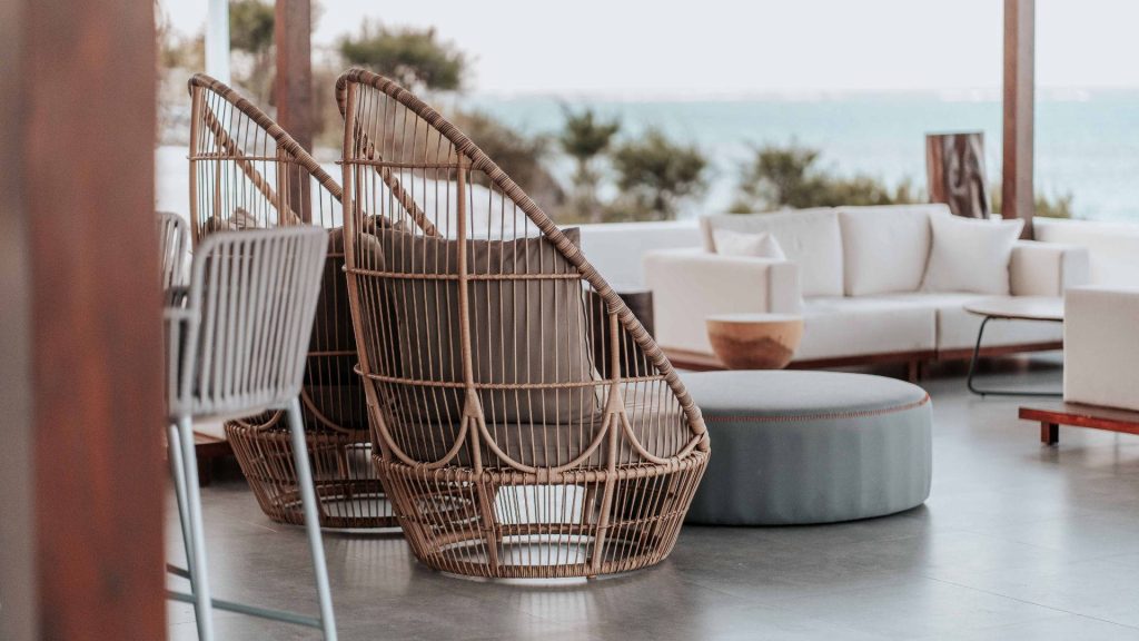 Luxury rattan Eden pod chairs with plush cushions in a serene coastal outdoor lounge setting Wallpaper