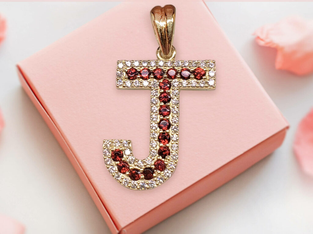 Elegant Ruby-Studded J Pendant on Soft Pink Background with Petals Wallpaper