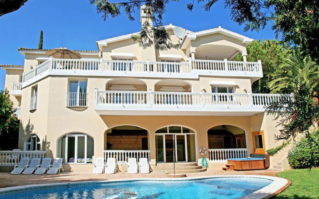 Luxurious beige three-storey villa with pool hot tub and lounge chairs in sunny serene setting Wallpaper