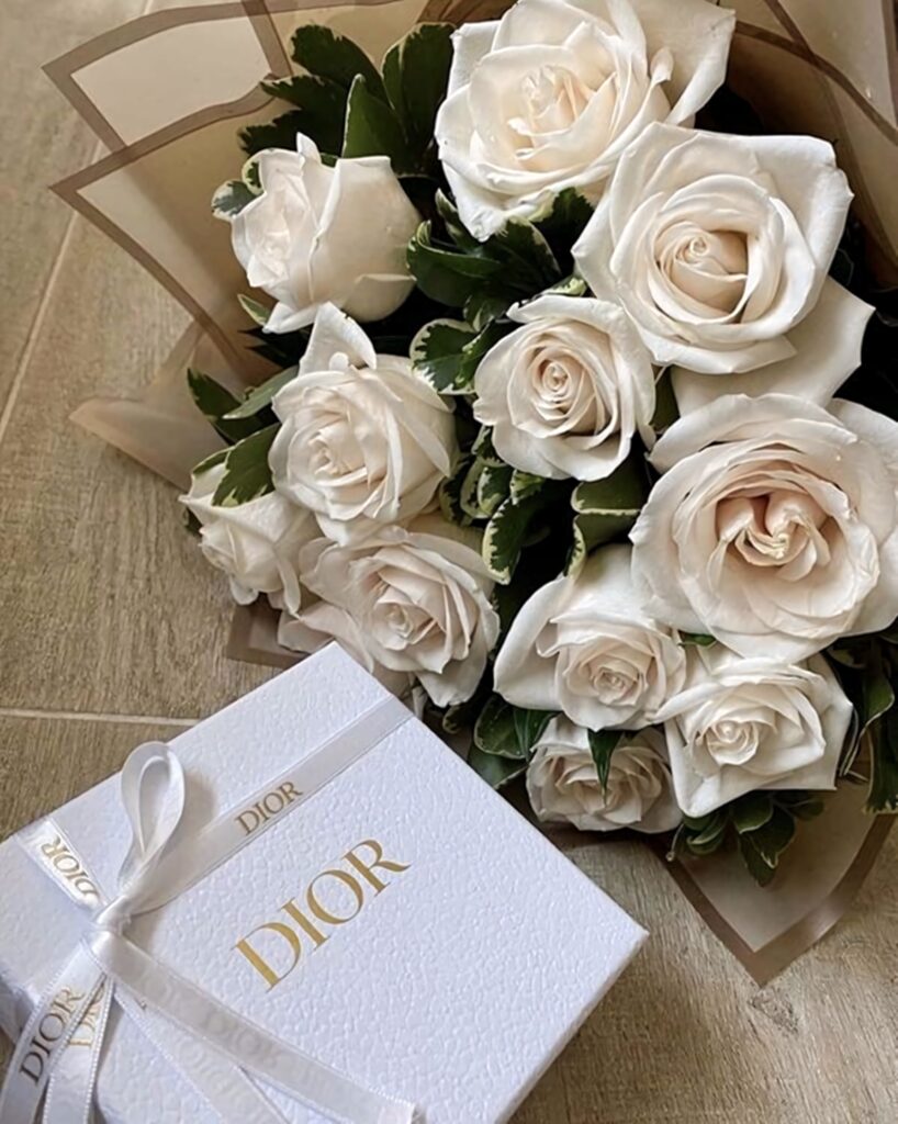 Luxurious white rose bouquet next to textured white Dior gift box with delicate ribbon background Wallpaper