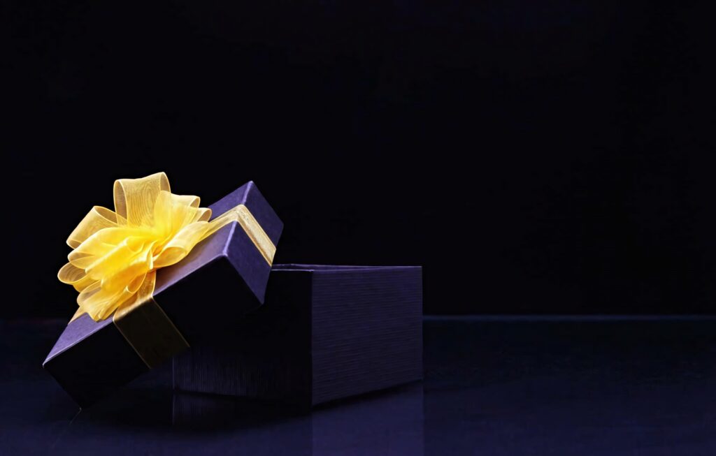 Black gift box with yellow ribbon partially open on dark elegant background luxury present Wallpaper