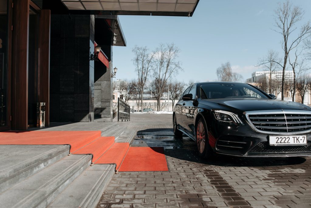 Luxury black Mercedes-Benz S-Class on vibrant red carpet at grand entrance in bright daylight Wallpaper