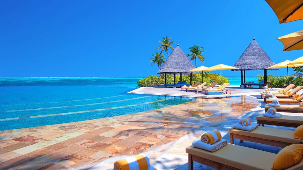 Luxury Maldives infinity pool with lounge chairs yellow towels thatched cabanas ocean view Wallpaper