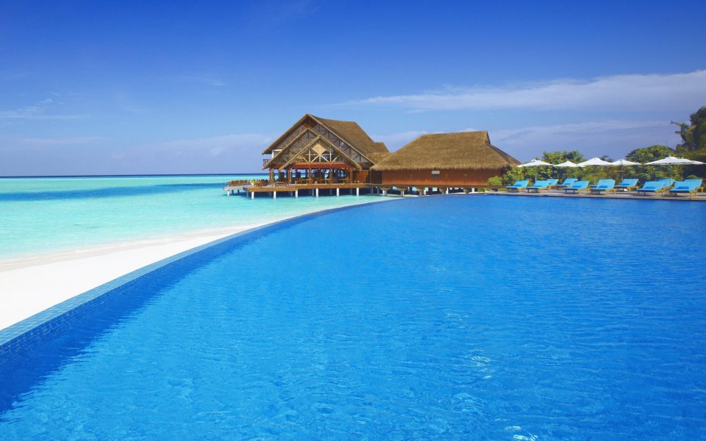 Luxury Maldives resort with infinity pool ocean view white sand beach and thatched roof bungalows Wallpaper