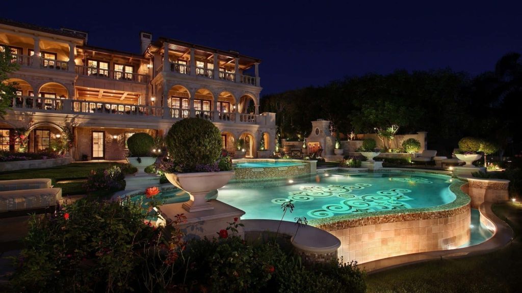 Luxury Mediterranean mansion at night with illuminated custom tiled freeform pool and warm lighting Wallpaper
