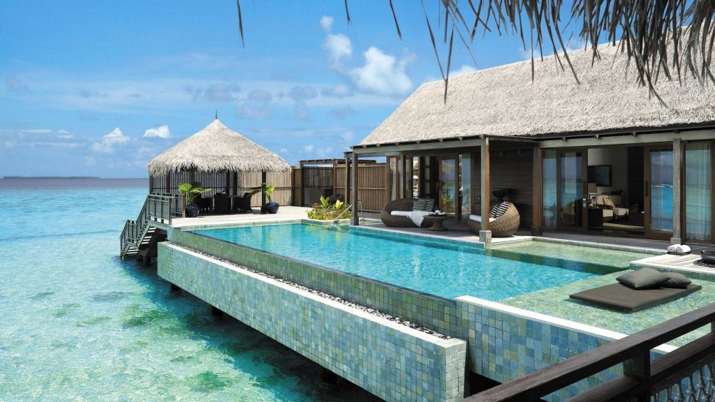 Luxury overwater villa with infinity pool overlooking turquoise ocean under sunny tropical sky Wallpaper