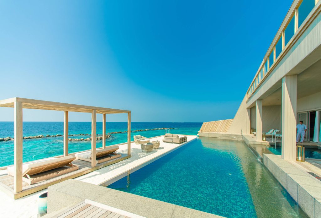 Scenic Patina Maldives infinity pool with wooden deck lounge chairs white sand turquoise ocean Wallpaper