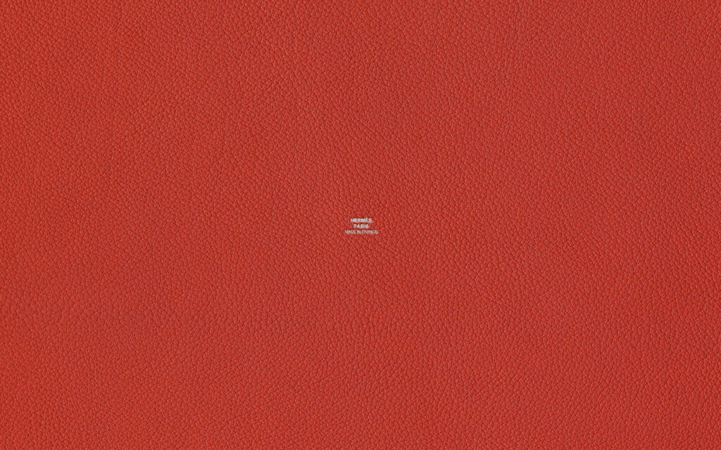 Vibrant red textured leather wallpaper with subtle pebbled pattern and small Hermes logo center