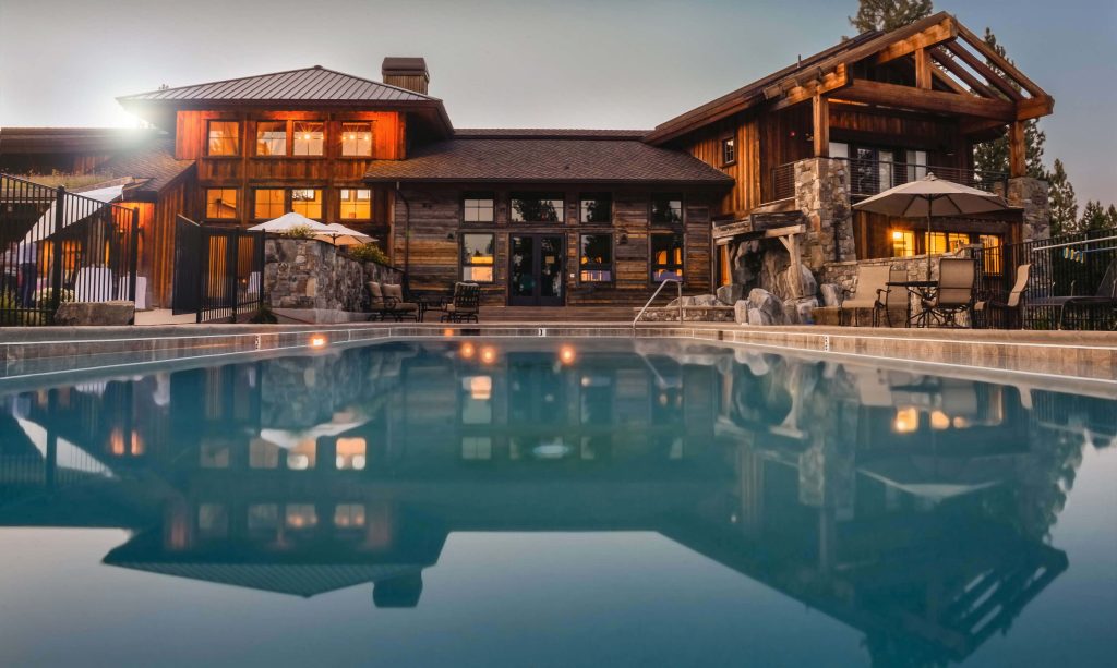Luxury timber stone house at dusk with glowing warm lights reflecting in calm pool wallpaper