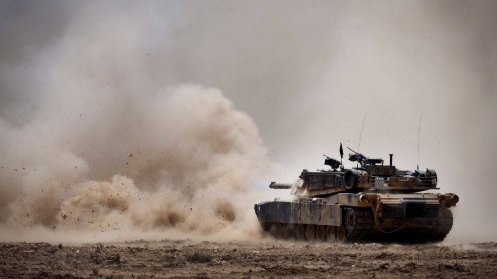 M1 Abrams tank charging through dusty field intense modern armored combat wallpaper background