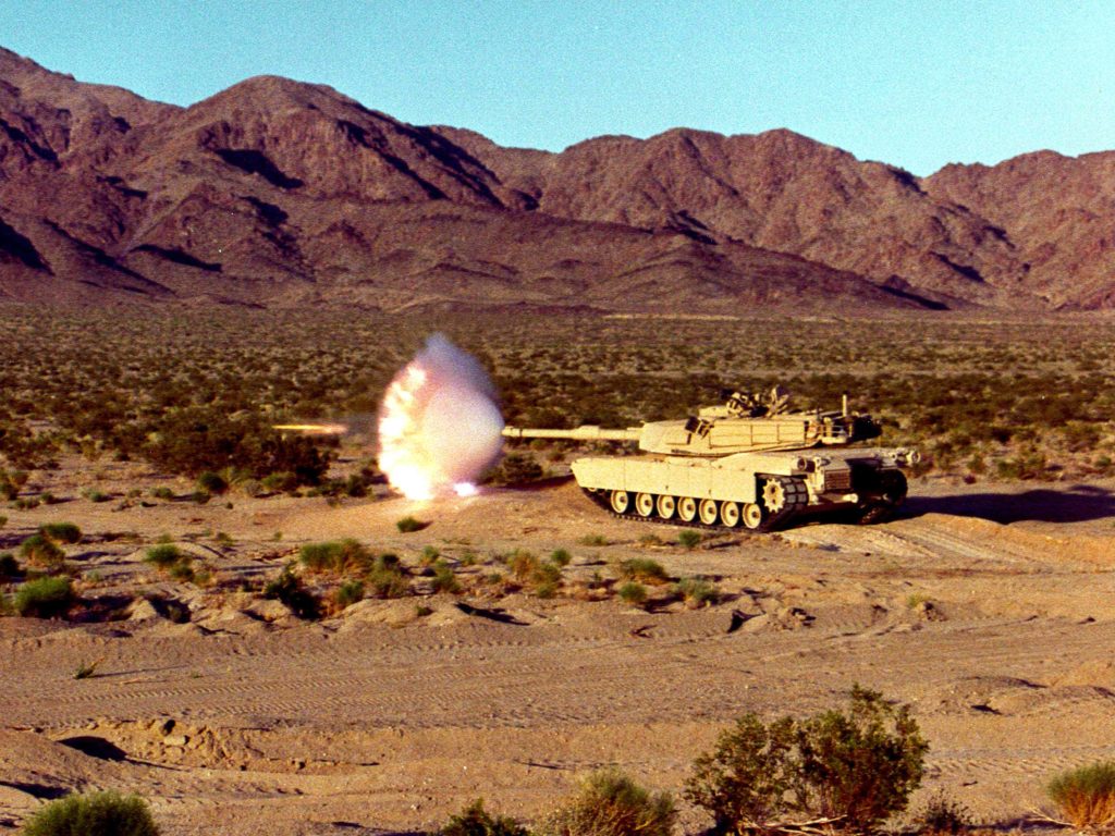 M1 Abrams tank firing main gun with muzzle flash in desert mountains high quality wallpaper