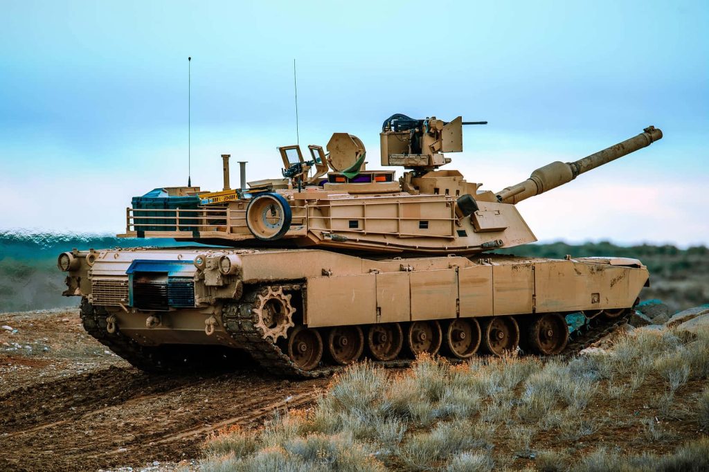 M1 Abrams tank in desert camo on rugged terrain under overcast sky military wallpaper background