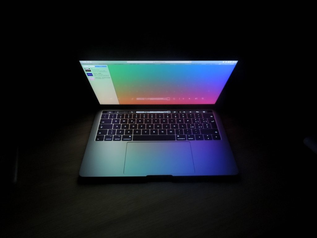 Open MacBook Pro with vibrant neon gradient display and illuminated keyboard on black background Wallpaper