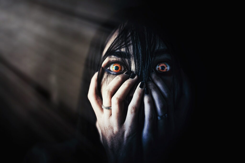 Spooky Horror Wallpaper: Person with Orange Eyes Peeking Through Shadowy Fingers