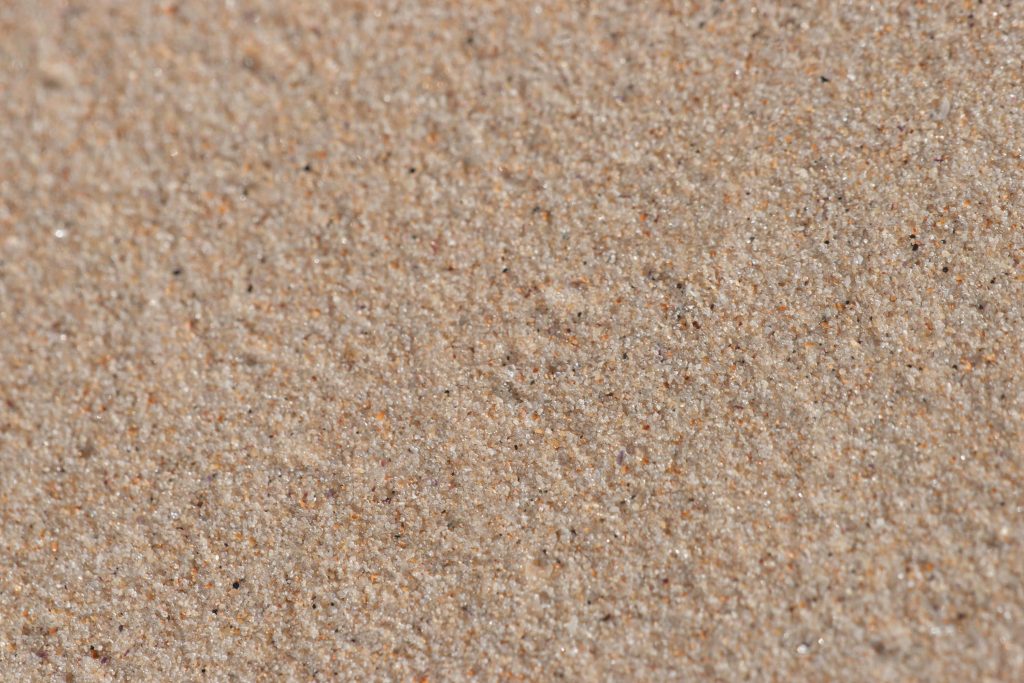 Macro close-up of fine beige sand with dark mineral flecks in natural sunlight beach texture Wallpaper