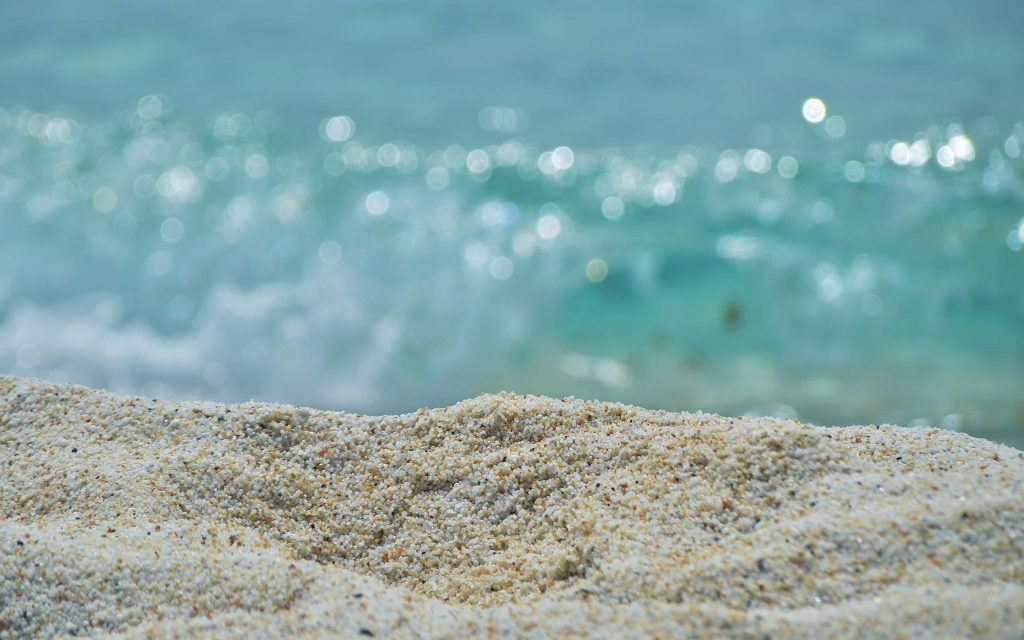 Macro beach sand texture with shimmering turquoise ocean waves and bright bokeh highlights wallpaper