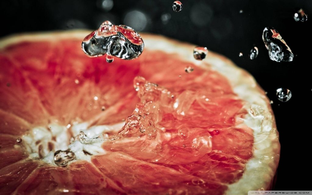 Close-up of juicy grapefruit slice with water droplets splash on dark background wallpaper