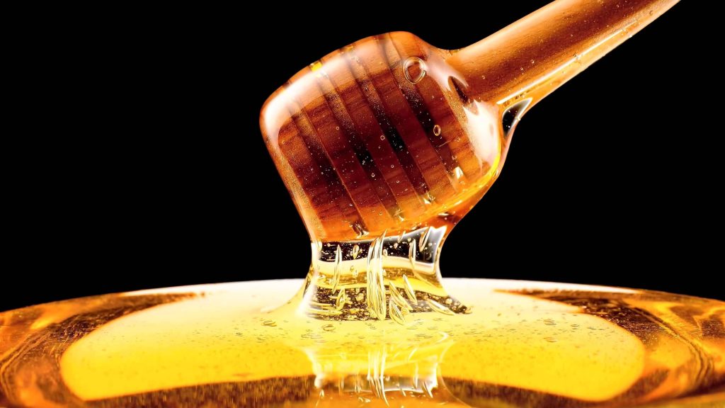 Macro shot of golden honey dripping from honey dipper into vibrant pool on black background Wallpaper