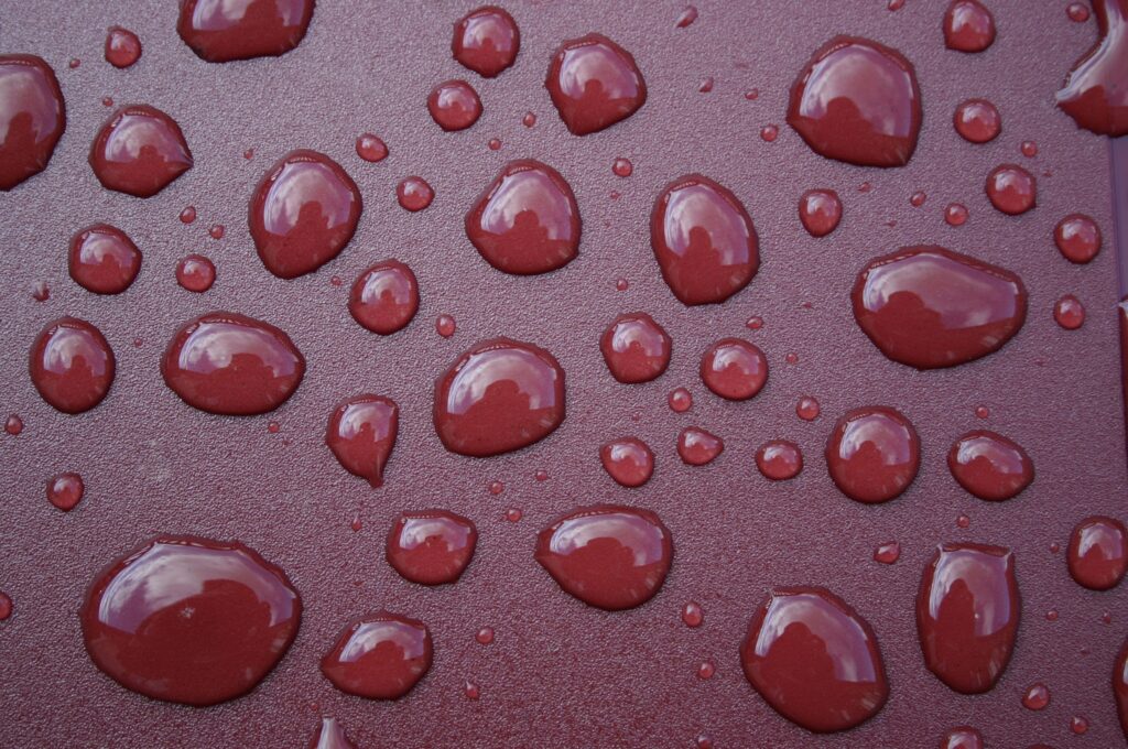 Macro Water Droplets on Textured Maroon Surface - Wallpaper Background