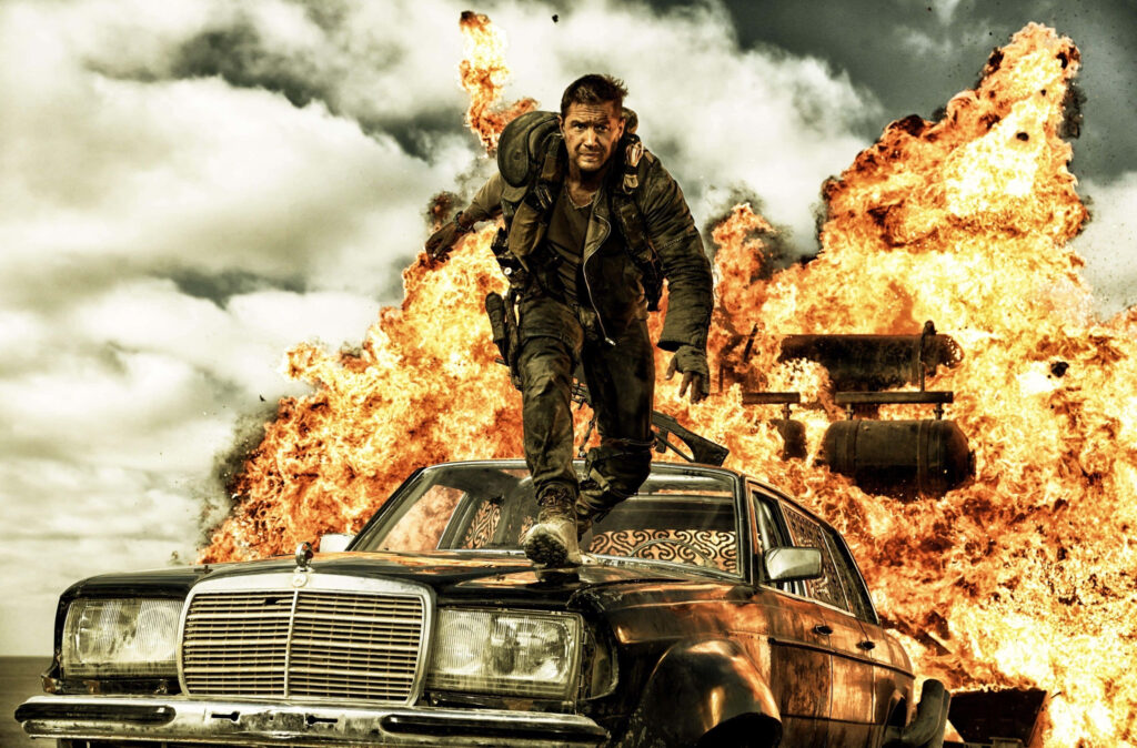 Mad Max racing battered car with massive explosions in chaotic post apocalyptic action wallpaper background