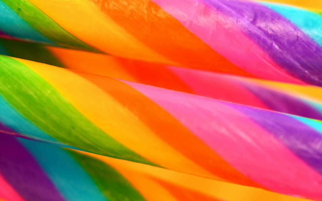 A Mesmerizing Candy Wonderland: Vibrant Rainbow-hued Candy Canes Embellished in Macro and Enhanced Glossiness Creating an Enchanting Background Design Wallpaper