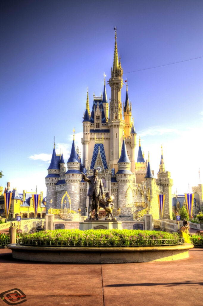 Disney Castle glowing in golden evening light surrounded by lush greenery and colorful banners Wallpaper