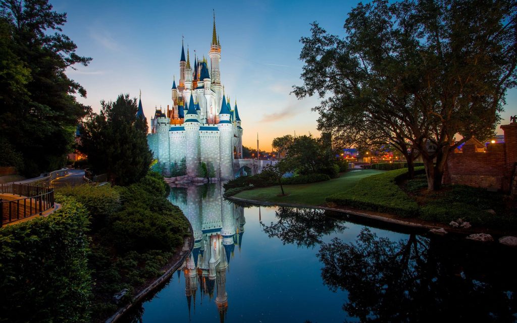 Cinderella Castle at Disney World glowing at twilight reflected in moat with lush trees wallpaper