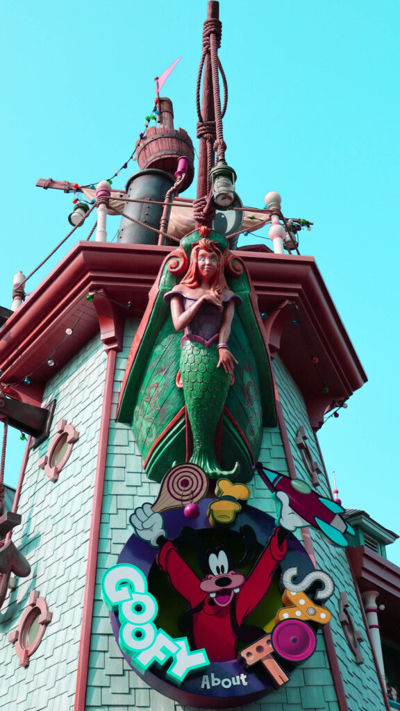 Colorful Disneyland wallpaper with mermaid statue and Goofy sign surrounded by sweets background