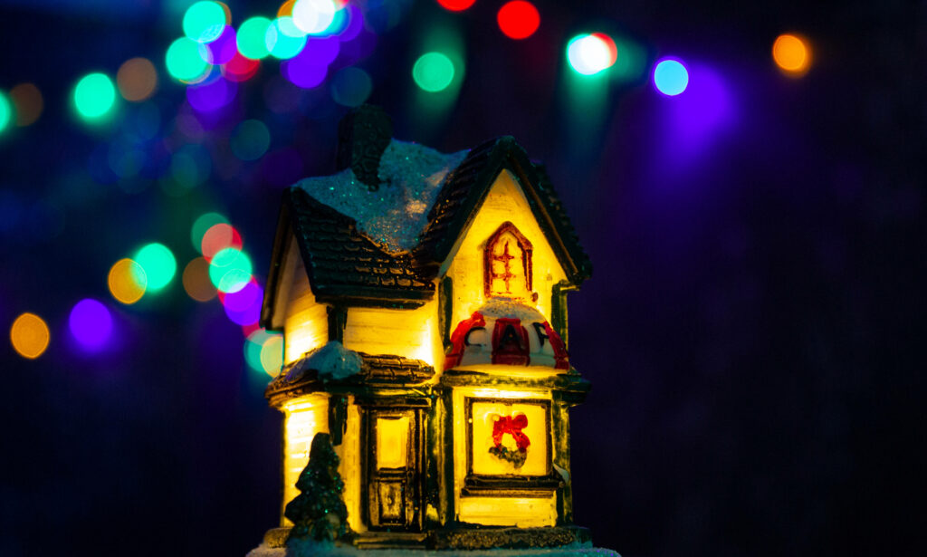 Enchanting Glow: Miniature Christmas House Radiates Warmth Against a Kaleidoscope of Colorful Illuminations Wallpaper