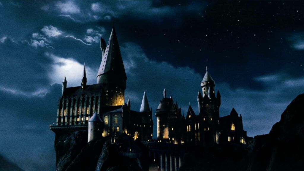 Hogwarts Castle glowing under starry night sky on cliff cinematic Harry Potter wallpaper background