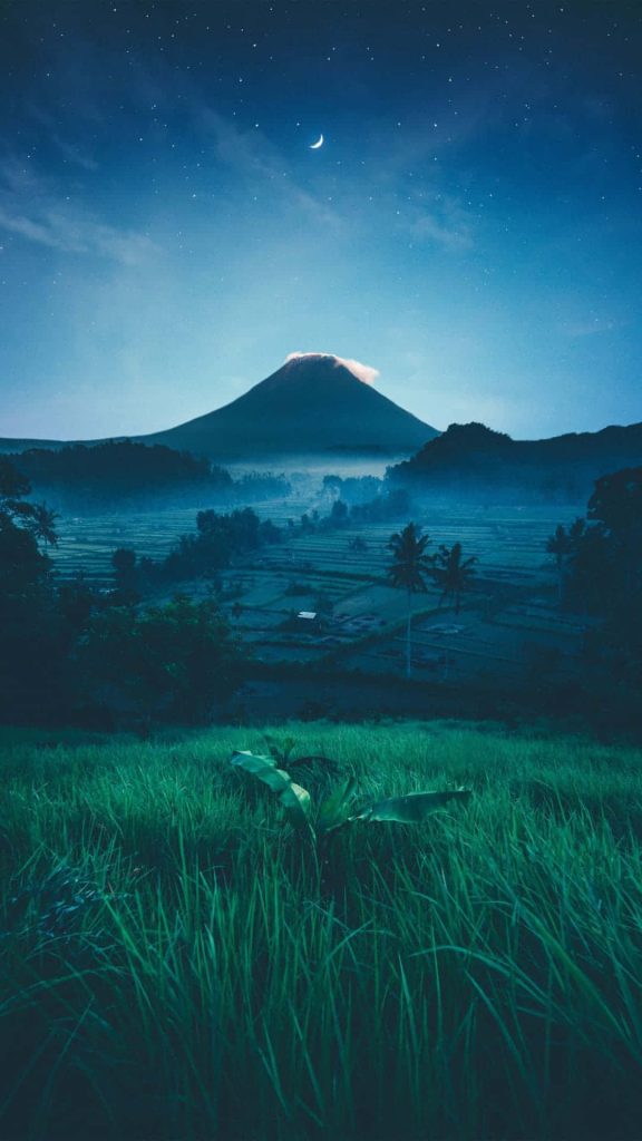 Night mountain view wallpaper with volcano lush terraces starry sky and crescent moon