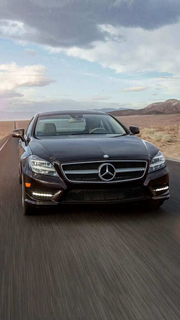 Mahogany Mercedes classic car driving on open desert road under dramatic cloudy sky wallpaper