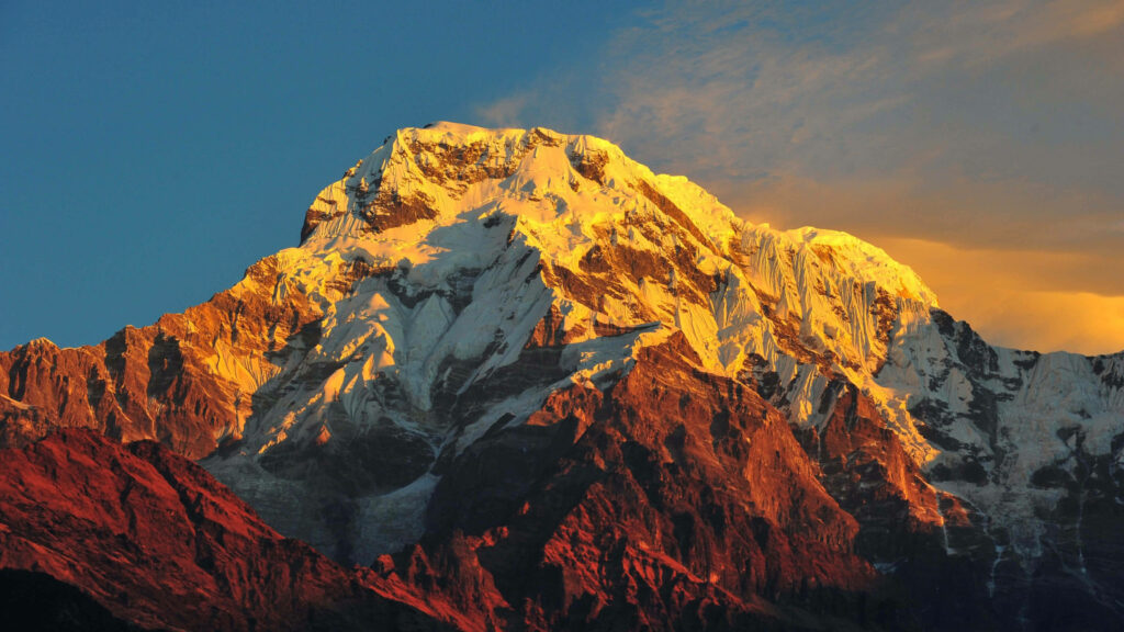 Majestic Annapurna Massif: A 4k Spectacle of Snowy Peaks and Rocky Slopes, Set Against a Mesmerizing Orange Sunset and Crystal Clear Blue Sky Wallpaper