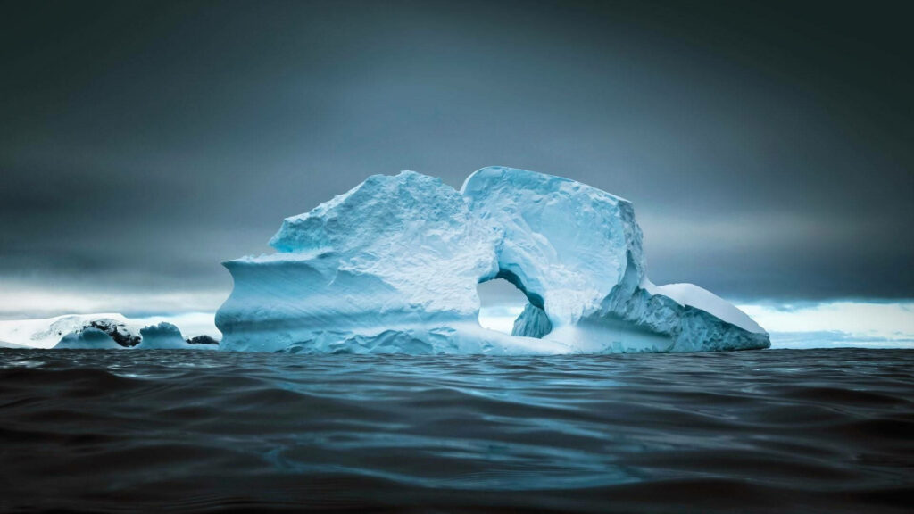 Massive Antarctic ice glacier rising from dark waters under dramatic cloudy sky wallpaper background