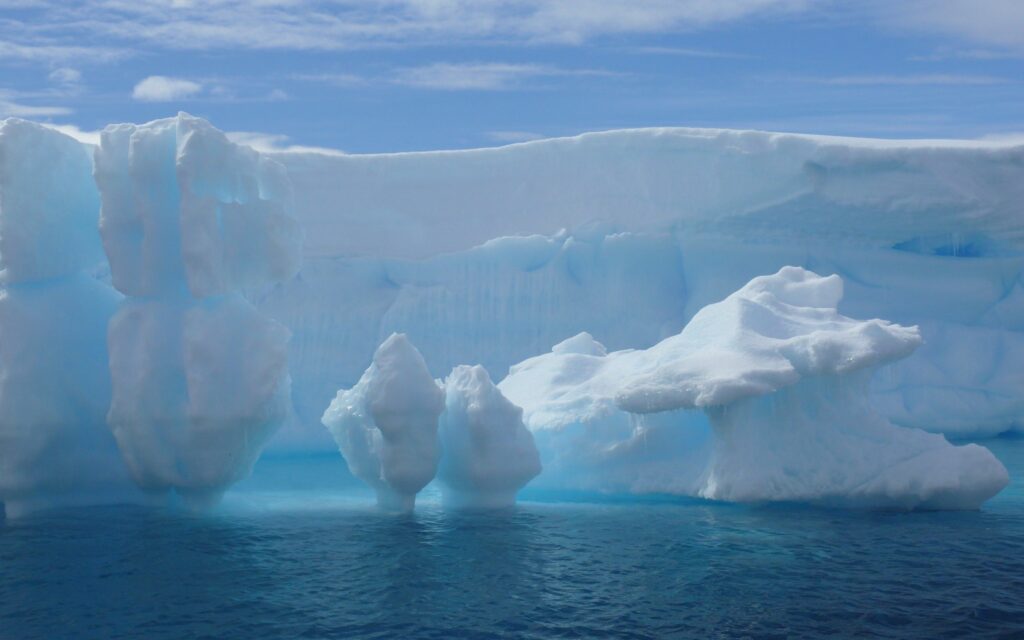 Massive glacier with intricate snow formations above deep blue ocean in serene Arctic landscape Wallpaper
