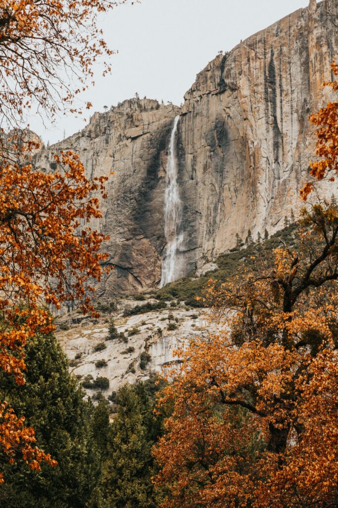 Dramatic cliff waterfall with vibrant golden autumn trees serene fall landscape wallpaper background