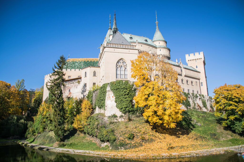 Bojnice Castle medieval architecture with autumn foliage and clear sky reflected in calm water Wallpaper