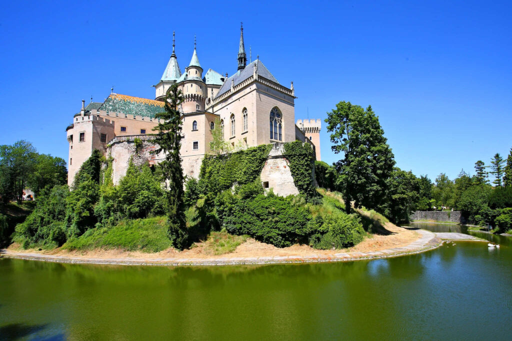 Bojnice Castle Slovakia medieval architecture lush greenery water moat vibrant blue sky wallpaper