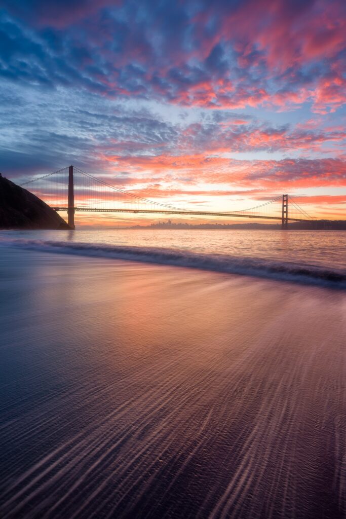 Majestic bridge silhouette at vibrant sunset with soft waves and colorful reflective water wallpaper